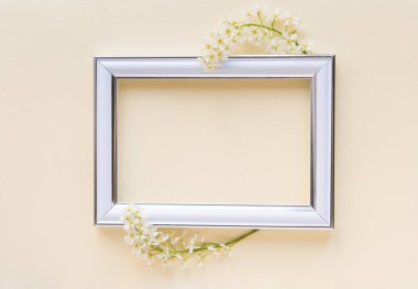 Beyaz kuş kirazının iki dalı boş beyaz bir fotoğraf çerçevesinin yanında sade, hassas bir pastel arka planda..