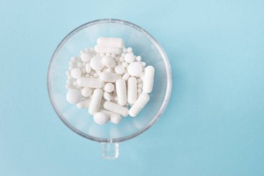 Farklı beyaz haplar ve mavi arka planda plastik bir kap. Tıbbi tema.