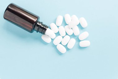 Mavi arka planda çeşitli beyaz haplar ve kahverengi plastik şişeler. Tıbbi tema.