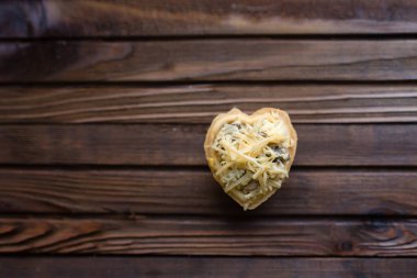 Tahta arka planda kalp şeklinde peynirli tart.