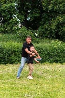 Baba ve oğlu yeşil çimlerin üzerinde eğlenceli açık hava sporları oynuyorlar. Babalar günü, aile günü..