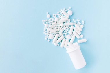 Farklı beyaz haplar ve mavi arka planda plastik bir kap. Tıbbi tema.