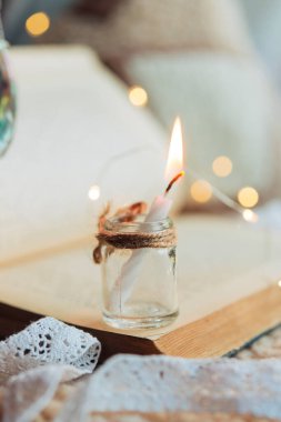 Eski açık bir kitabın arka planında cam bir kavanozda mum yakmak. Arka planda tatil ışıkları yanar.