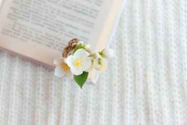 Beyaz örülmüş arka planda açık bir kitaptaki bulanık cam vazoda bir buket beyaz çiçeğin yakın çekimi. Yavaş yaşam konsepti.