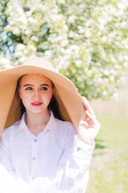 # Hasır şapkalı genç bir kız ve beyaz bir bluz # # Çiçek açan bir ağacın arka planında #