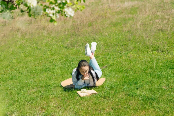 Dziewczyna Białej Bluzce Niebieskich Dżinsach Leżąc Parku Trawie Czytając Książkę — Zdjęcie stockowe