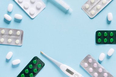 Minimalist tıp ve sağlık konsepti yassı haplar ve mavi arka planda bir termometre.