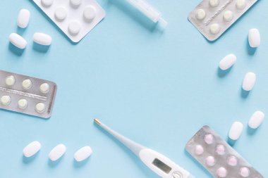 Minimalist tıp ve sağlık konsepti yassı haplar ve mavi arka planda bir termometre.