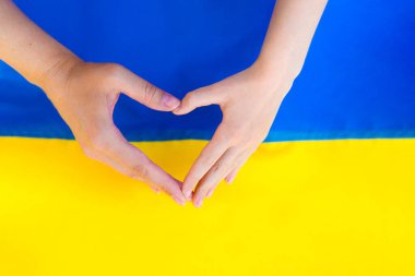 Kadın ve çocukların elleri Ukrayna bayrağının önünde bir kalp gösteriyor. Ukrayna bayrağının dokusu. Ukrayna sembolleri. Savaş 2022.