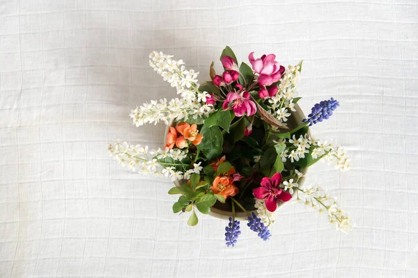 Summer blooming delicate flowers in a round vase on a table with a white tablecloth, a pastel bouquet and a delicate floral card