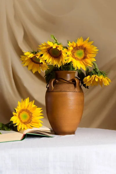 Bouquet of sunflowers in an old earthenware jug. In the foreground is an open book and a flower.
