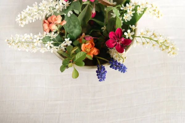 Summer blooming delicate flowers in a round vase on a table with a white tablecloth, a pastel bouquet and a delicate floral card