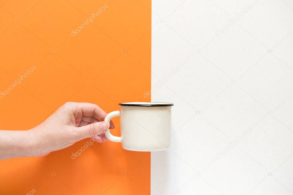 woman's hand holds a white cup. View from above. A cup on an orange and gray background. copy space for text
