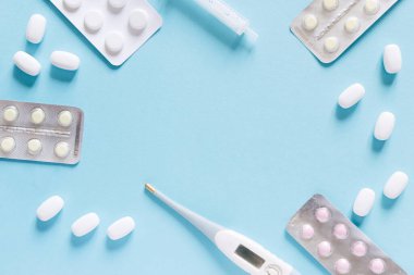 Minimalist tıp ve sağlık konsepti yassı haplar ve mavi arka planda bir termometre.