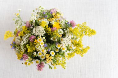 Yaz çiçekleri yuvarlak bir vazoda beyaz bir masa örtüsü, pastel bir buket ve narin bir çiçek kartıyla açıyor.