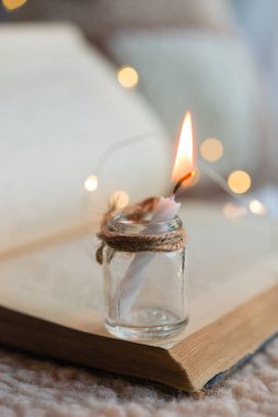 Eski açık bir kitabın arka planında cam bir kavanozda mum yakmak. Arka planda tatil ışıkları yanar.