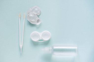 Contact lenses set with saline in bottle, tweezers, plastic case with solution on blue background with copy space