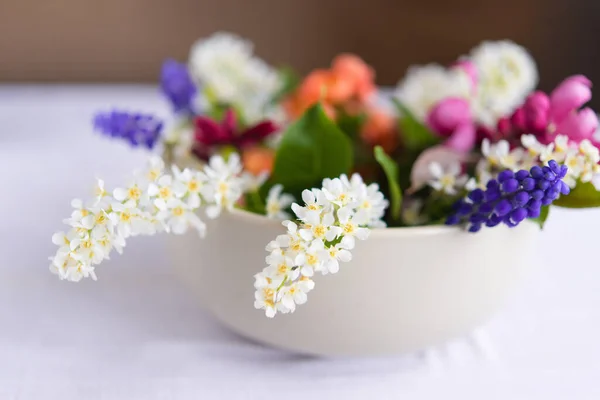 Spring blooming delicate flowers in a round vase on a table with a white tablecloth, a pastel bouquet and a delicate floral card