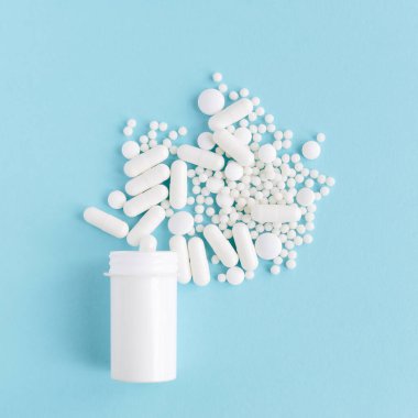 Farklı beyaz haplar ve mavi arka planda plastik bir kap. Tıbbi tema.