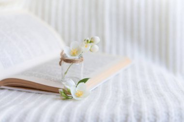 Beyaz örülmüş arka planda açık bir kitaptaki bulanık cam vazoda bir buket beyaz çiçeğin yakın çekimi. Yavaş yaşam konsepti.
