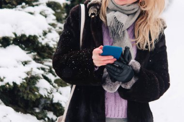 Kış manzarası, karda Noel ağaçları. Cep telefonlu kadın fotoğrafı çekiliyor ve çevresindeki doğayı gösteriyor..