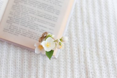 Beyaz örülmüş arka planda açık bir kitaptaki bulanık cam vazoda bir buket beyaz çiçeğin yakın çekimi. Yavaş yaşam konsepti.
