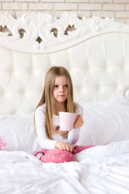 Küçük tatlı kız yatakta kahvaltı yapıyor. Kız elinde bir bardak tutuyor. ışık içerisi.