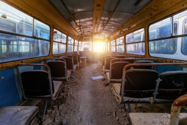 Terk edilmiş eski, paslı hurda otobüs ya da troleybüsün içinde.