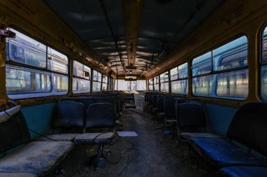 Terk edilmiş eski, paslı hurda otobüs ya da troleybüsün içinde.