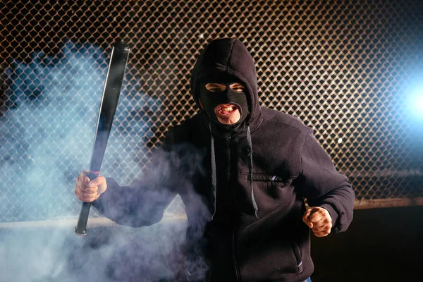 Masked angry man with bat in smoke.