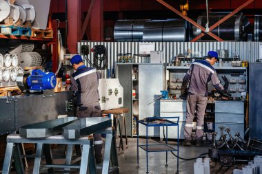 Fabrika işçileri atölyede metal ekipman monte ediyorlar.