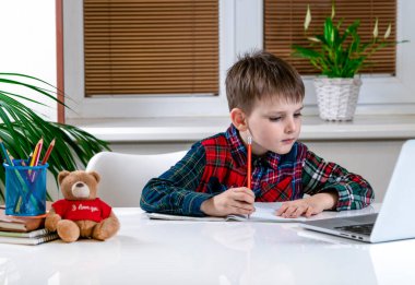 Küçük çocuk evde, masada ödev yapıyor.