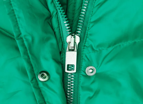 Fragment of a green jacket made of waterproof fabric with seams, metal button and opened zip fastener
