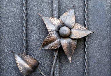 Güzel, eski, dövülmüş metalin yakın plan detayları. Büyük, sarı ve kırmızı çiçek. Demir, gri çitleri süslüyor.