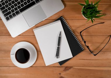Sade kahve ve dizüstü bilgisayarlı ahşap masa, defter ve gözlük.