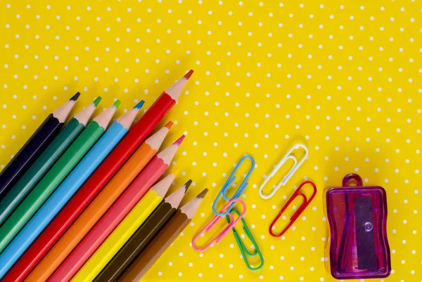 Rainbow color pencils, sharpener and paper clips on yellow background