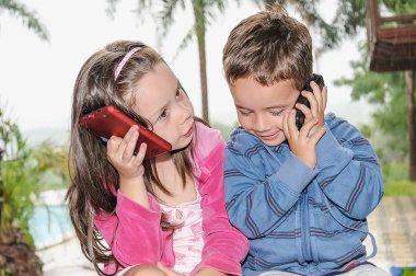 küçük kız ve oğlan bir cep telefonu ile bir parkta