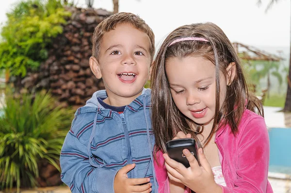 Malou holčičku a chlapce v parku s mobilním telefonem — Stock fotografie