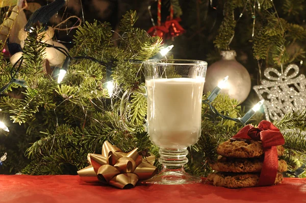 Melk med kjeks og gyllen bue under juletreet – stockfoto