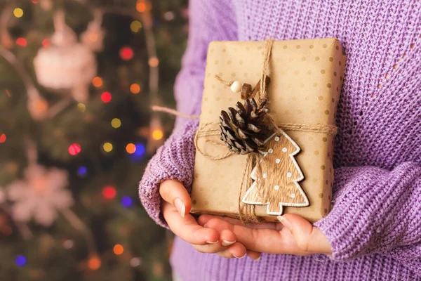 Dívka drží malý dárek ve svých rukou. zdobené vánoční stromeček na pozadí. Světlé vánoční přání s prostorem pro text — Stock fotografie