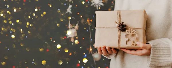 Mädchen mit kleinem Geschenk in der Hand. geschmückter Weihnachtsbaum im Hintergrund. Helle Weihnachtskarte mit Platz für Text — Stockfoto