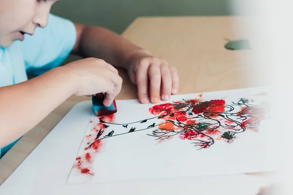 Anak lucu duduk di meja dan membuat gambar dari daun birch berwarna kering — Stok Foto