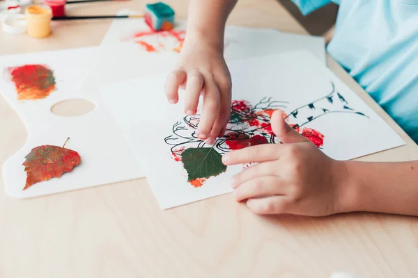 Schattig kind zittend aan bureau en het maken van foto 's van droge berkenbladeren — Stockfoto