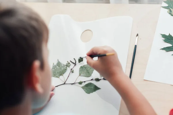Anak manis duduk di meja dan membuat gambar dari daun birch kering — Stok Foto