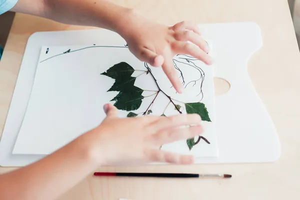 Anak manis duduk di meja dan membuat gambar dari daun birch kering — Stok Foto