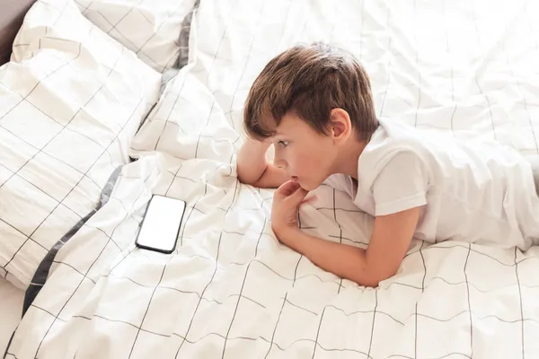 Anak duduk santai di tempat tidur dan bermain di smartphone — Stok Foto