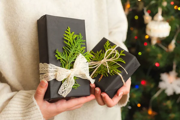 A nő apró ajándékokat tart a kezében. díszített karácsonyfa a háttérben — Stock Fotó