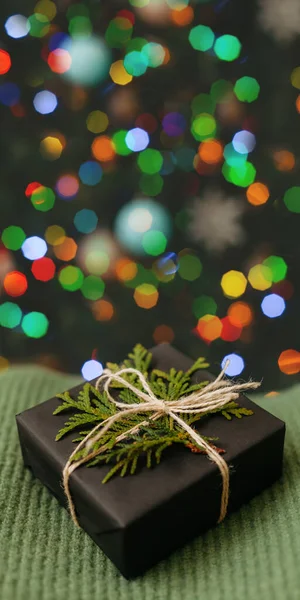 Pequeño regalo que pone en textil verde, árbol de Navidad decorado en el fondo. Tarjeta de Navidad brillante con espacio para el texto —  Fotos de Stock