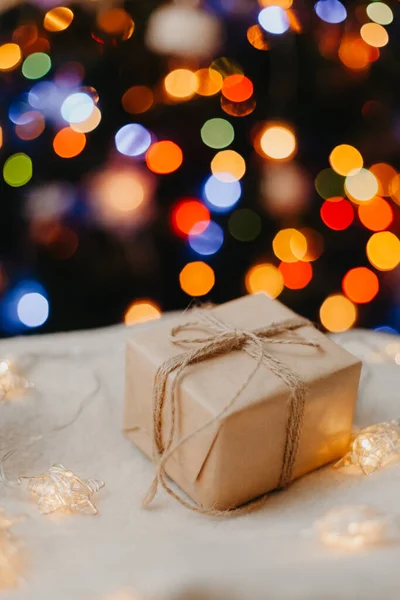 Malý dárek ležel na bílém svetru, zdobené vánoční stromeček na pozadí. — Stock fotografie