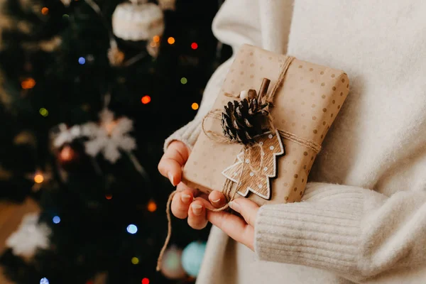 Mädchen mit kleinem Geschenk in der Hand. geschmückter Weihnachtsbaum im Hintergrund. Helle Weihnachtskarte mit Platz für Text — Stockfoto